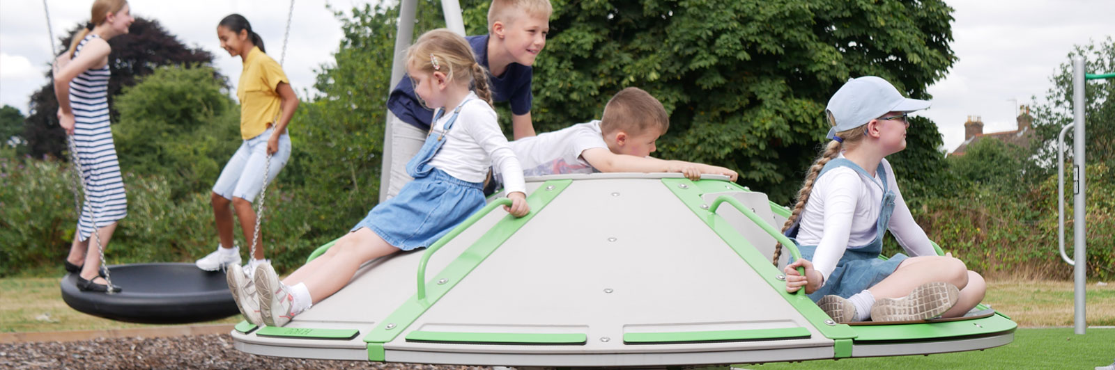 Children spinning on a roundabout while older children swing in the background